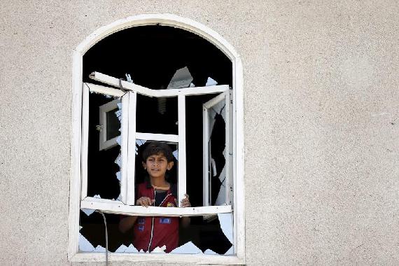A Yemeni child looking out a window shattered by explosions from air strikes