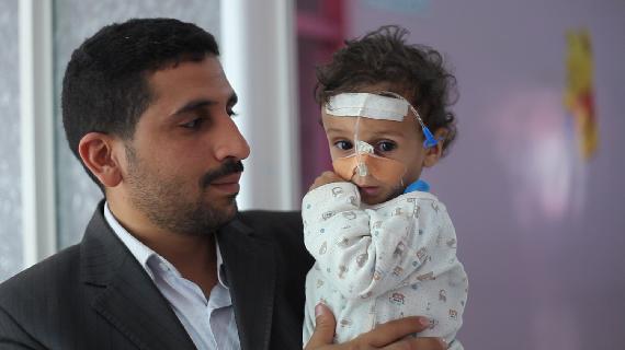 A father holding his sick child in the Malnutrition Ward in Al-Sabeen Maternity and Child Hospital