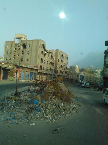 Debris from shelling piled in the street, while in the background are buildings pitted with shell strikes.